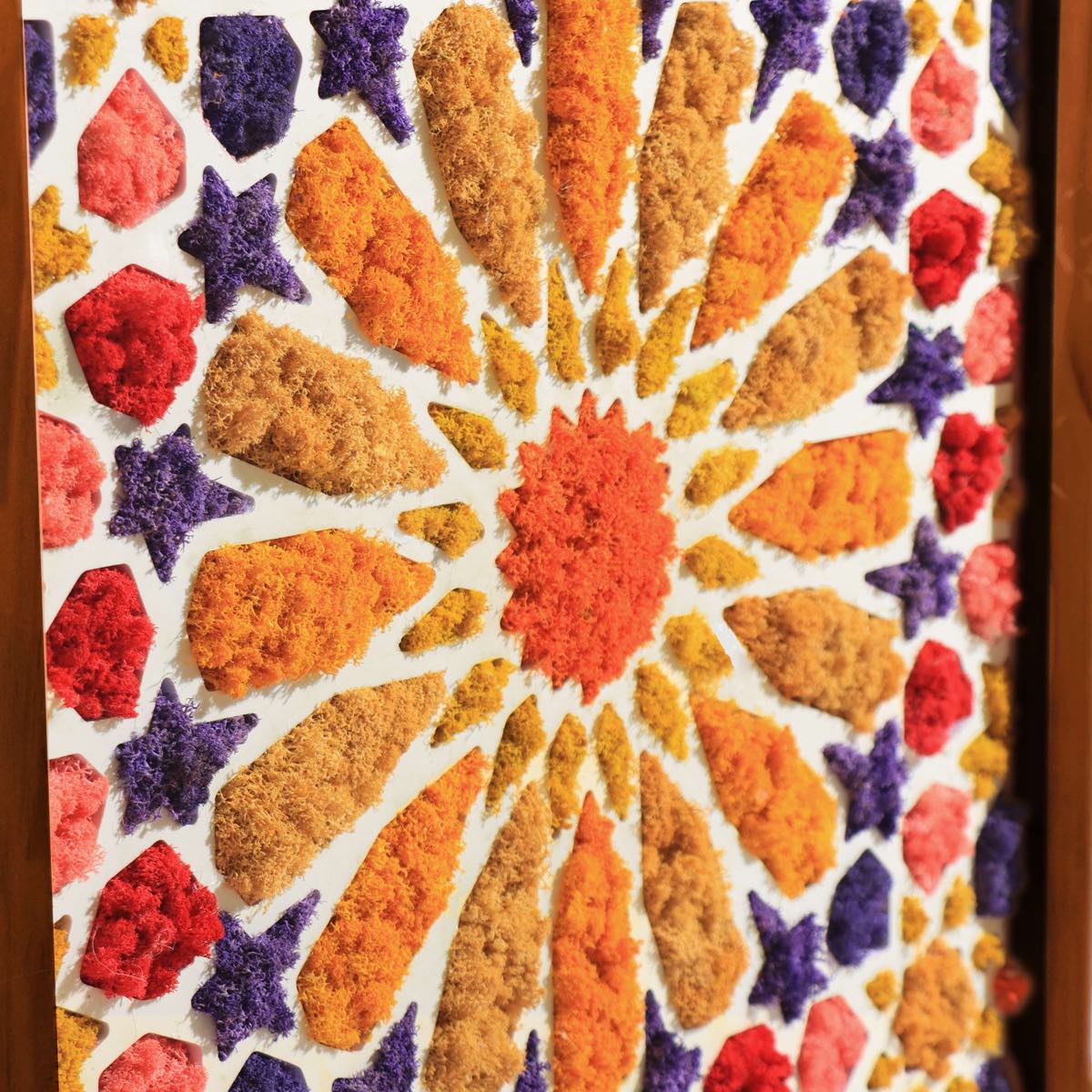 Close-up of arched Moroccan moss wall art featuring yellow, orange, and purple preserved moss in a geometric pattern.