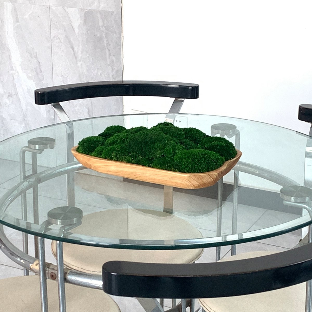 Live edge wooden moss bowl with preserved green moss displayed on a glass table in a modern office meeting space.