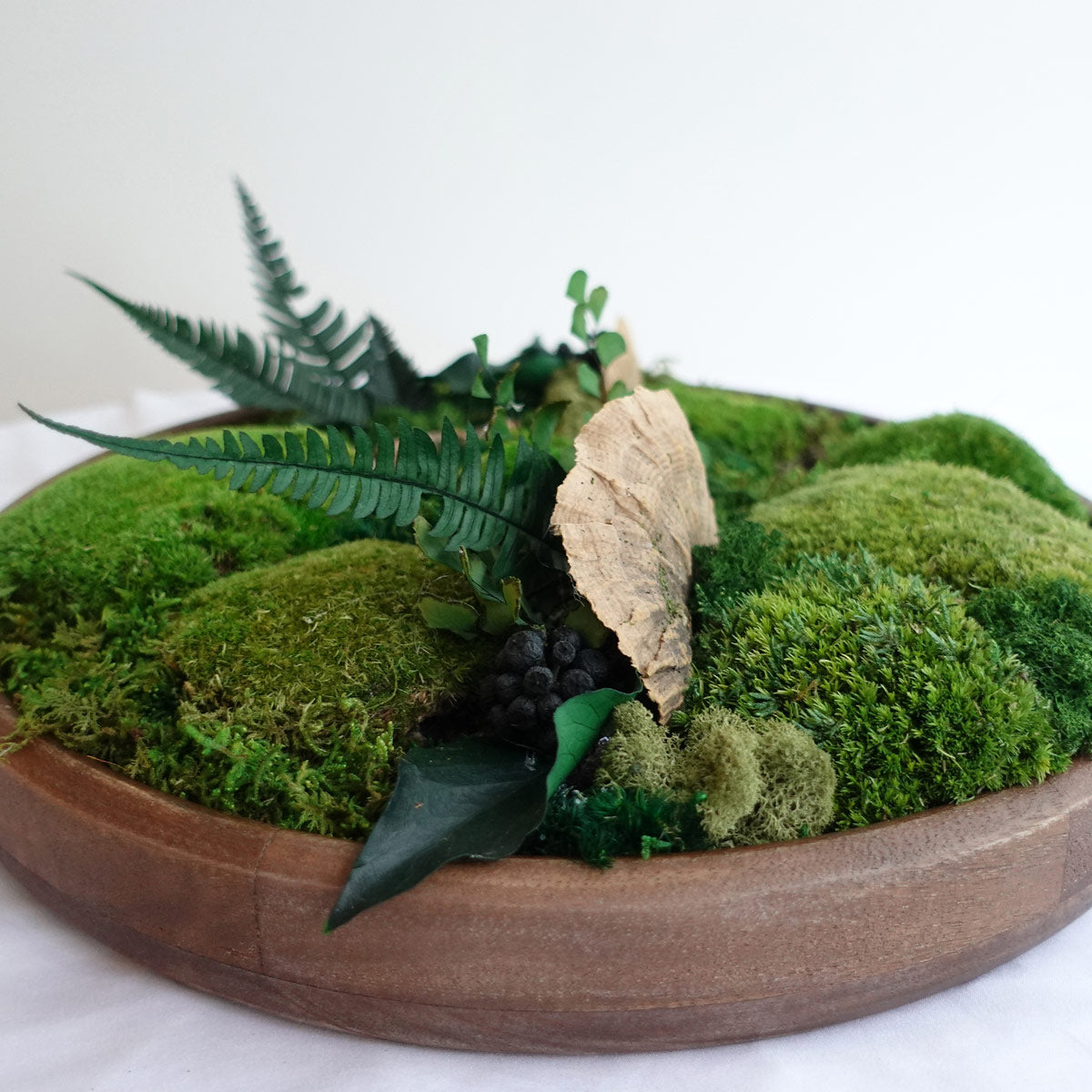 Side view of a preserved moss bowl with layered green moss, fern accents, and natural wood textures