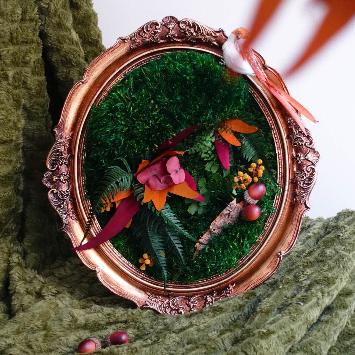Vintage oval framed moss art featuring preserved green moss with autumn foliage accents and a decorative bird, styled as seasonal wall decor.