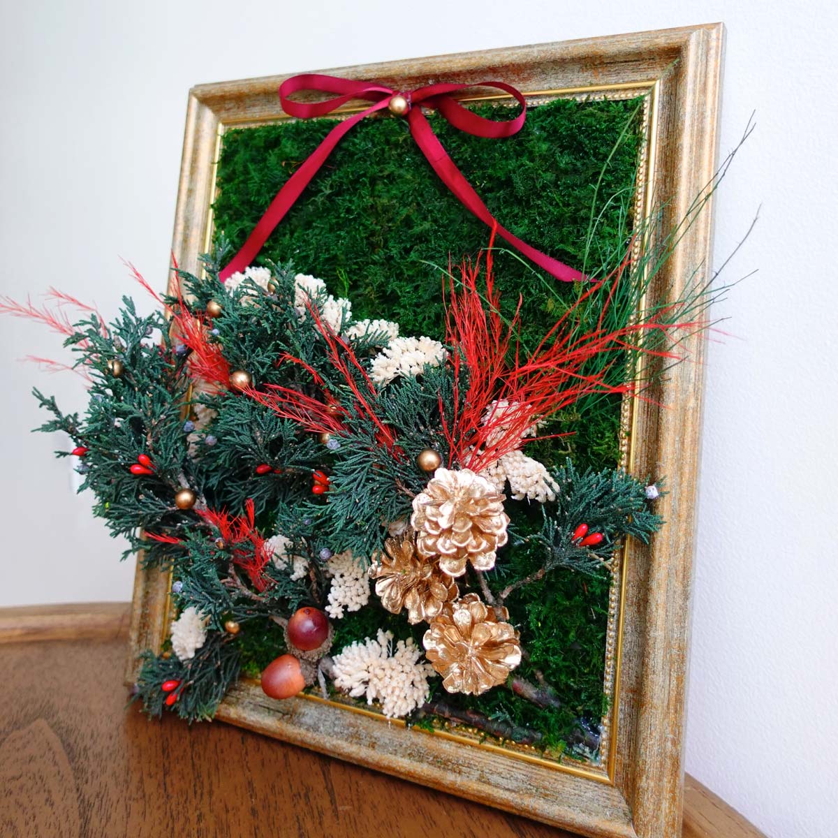 Antique gold framed Christmas moss wall art featuring preserved green moss, seasonal greenery, pinecones, and a red ribbon for holiday decor.