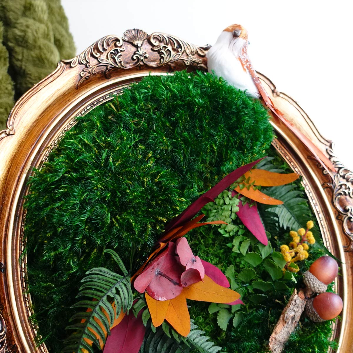 Close-up of vintage oval framed autumn moss art with preserved moss, dried florals, acorns, and textured antique frame details.